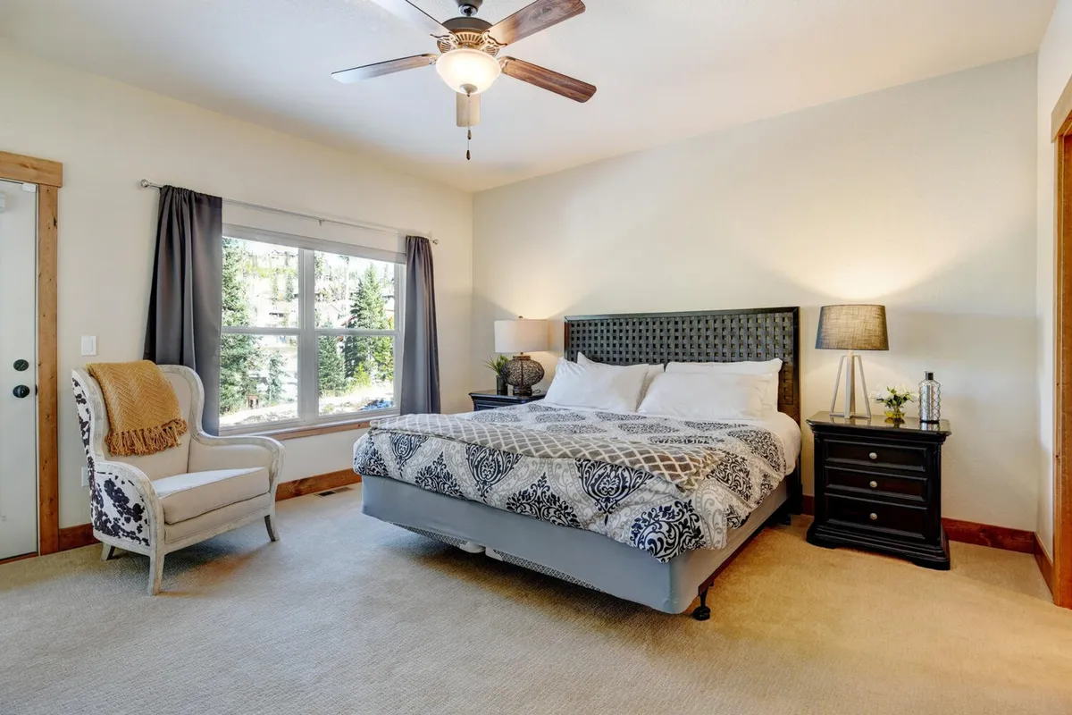 A serene bedroom featuring a bed with patterned bedding, a large window letting in natural light, and a nightstand with a cozy lamp. The overall atmosphere is calm and inviting, ideal for relaxation and restful nights.