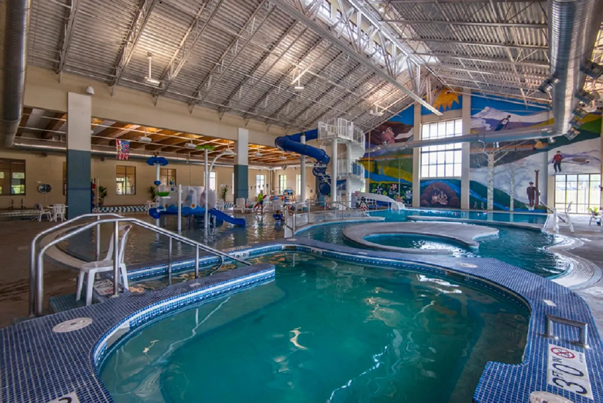 This image captures the vibrant pool area inside the Grand Park Rec Center, featuring a colorful water slide and active children playing in and around the water. The space is lively and filled with energy, clearly designed for all-ages fun and family gatherings.
