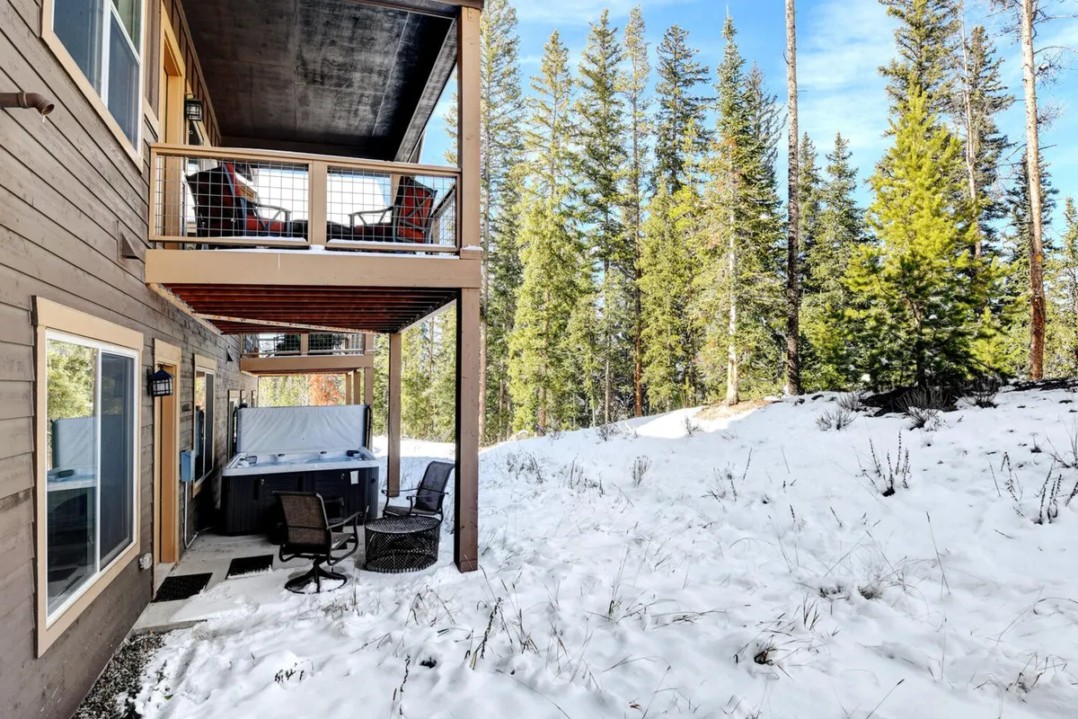 This exterior image shows a hot tub on a deck, complemented by an additional outdoor seating area and a balcony above. Snow is visible, suggesting year-round enjoyment, with possibilities for both stargazing and playful winter activities.