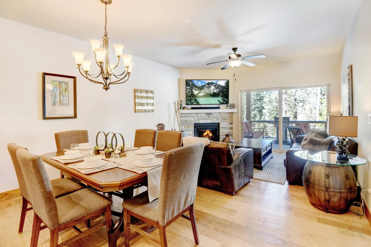 A beautifully set dining table sits adjacent to a fireplace and a plush seating area, all framed by a large window offering stunning views of the outdoors. The inviting atmosphere is enhanced by natural light and well-chosen decor.