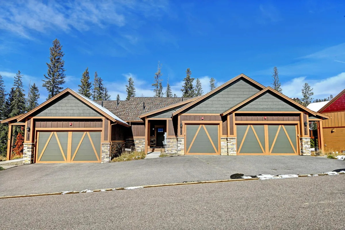 This exterior image showcases the front entrance of the home, framed by garage doors, stone accents, and an inviting yard. The lighting and landscaping create a welcoming atmosphere, and the open space hints at accessibility to neighborhood trails and outdoor exploration.