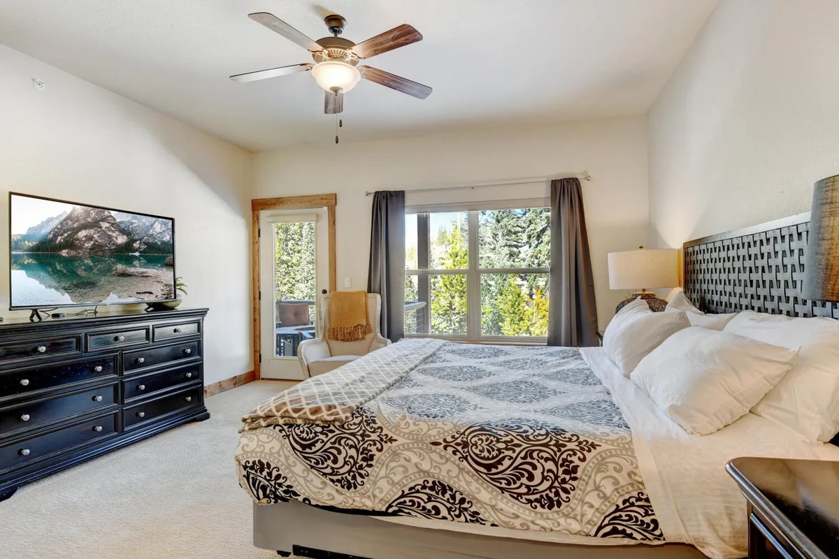 A tranquil bedroom with a comfortable bed adorned with decorative bedding, a large TV, and a window offering views of the outdoors. The space feels both modern and cozy, inviting relaxation after a day of adventure.