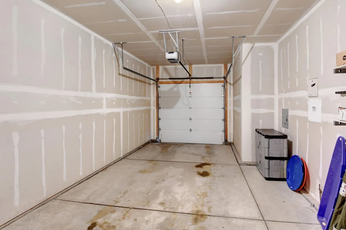 This image shows the interior of the garage, complete with a visible garage door, ceiling-mounted opener, and practical storage bins along the side. The scene is uncluttered and clearly focused on storage and organization, providing a functional backdrop ideal for staging outdoor gear such as skis, bikes, and boots.