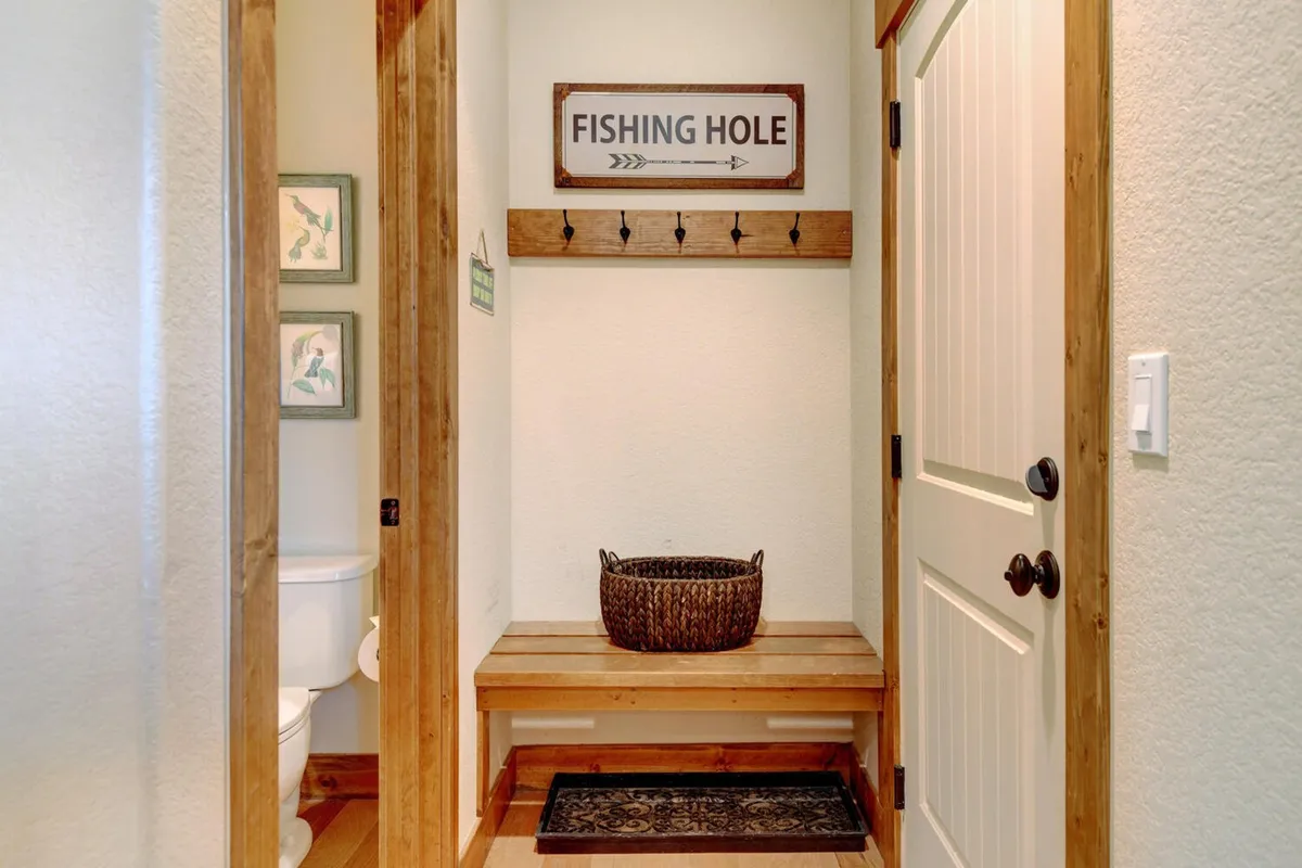 This entryway image features a wooden bench, woven basket, coat hooks, and a decorative 'Fishing Hole' sign. The space feels warm and inviting, perfect for removing boots, hanging jackets, and prepping for outdoor adventures. It signals a welcoming spot to transition from outside to inside.