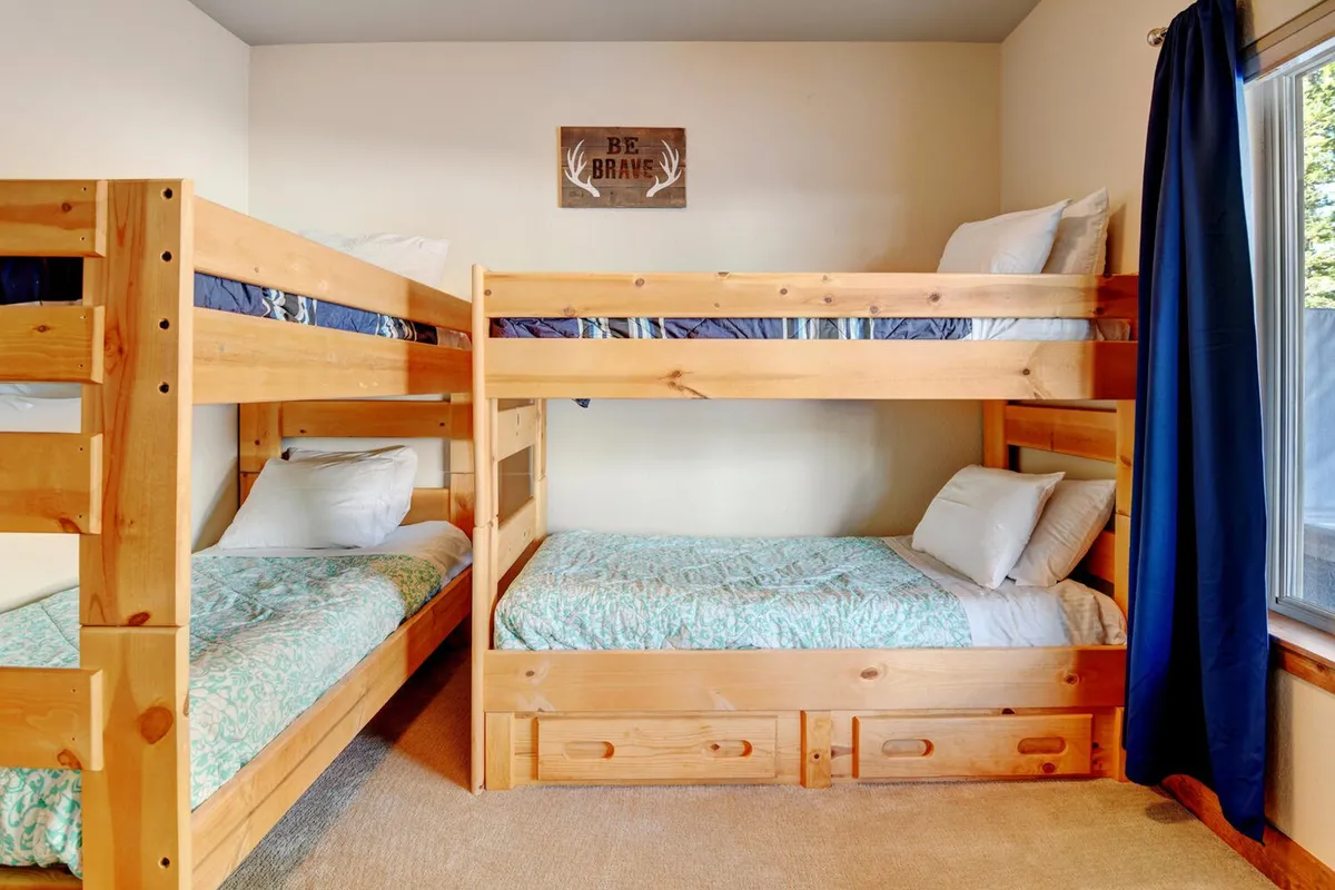 A cozy and playful kids’ bedroom featuring bunk beds, cheerful wall art, and a window letting in natural light. The space feels inviting for families, encouraging bedtime stories or playful moments.