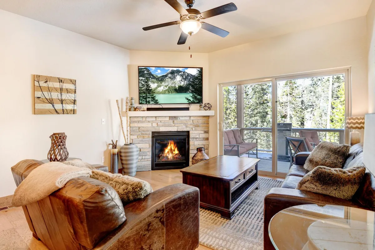 A cozy living room layout featuring a fireplace, a large smart TV with mountain views through a window, and comfortable sofas arranged for socializing or relaxing after a day of adventure.