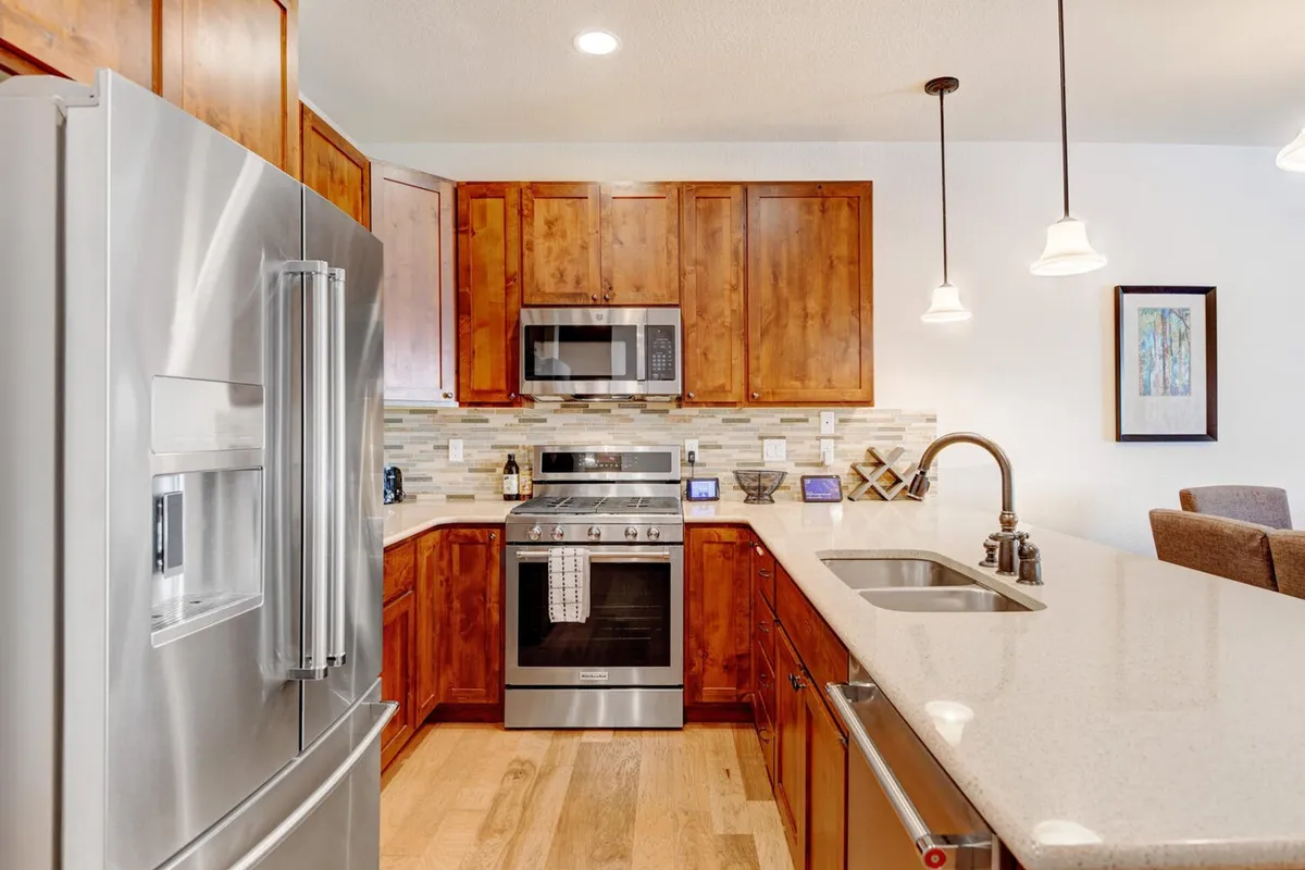A sleek, modern kitchen with stainless steel appliances, granite countertops, and warm wooden cabinetry. The layout suggests ease of movement and plenty of space for group cooking or entertaining.
