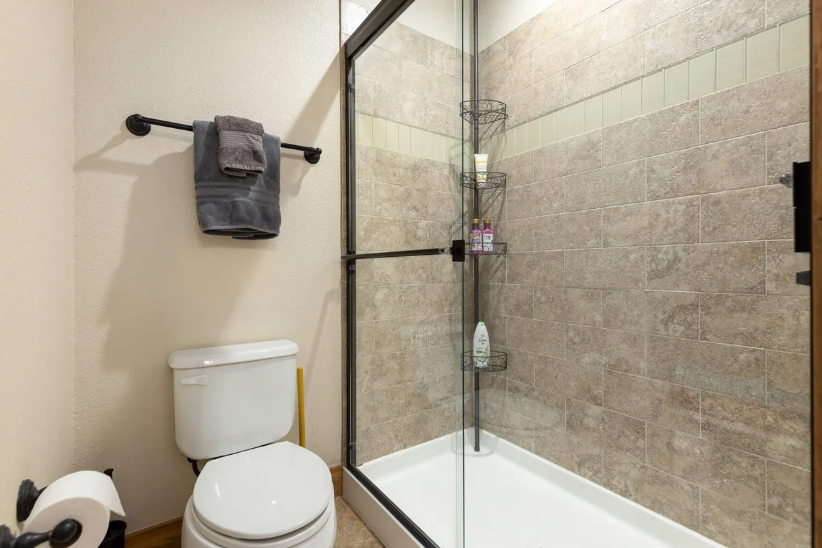 A spa-like bathroom featuring a glass shower enclosure, fresh towels on a rack, a toilet, and a shower caddy with personal care products. The design is clean and inviting, promising a rejuvenating experience.