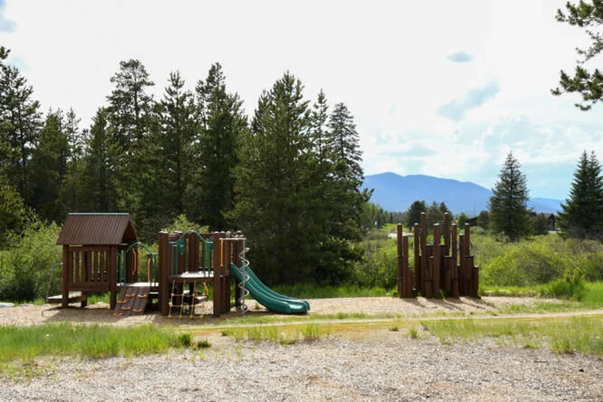 The image features a children’s playground structure with slides, set against a backdrop of mountains and surrounded by trees. Children can be seen playing, evoking the energy and joy of outdoor family fun. The Rec Center playground is visible, directly relating to the section's note about amenities for little ones.
